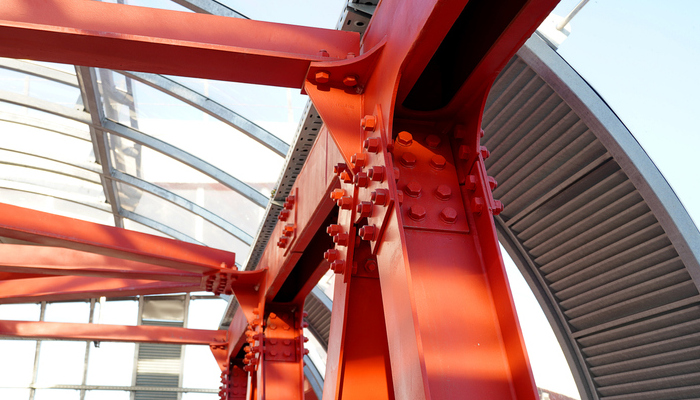 Red iron beams bolted on. Connection of several iron beams in one place. Indoor overhead pedestrian crossing with iron construction and glass ceiling.